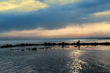 Gün batımı, alçak deniz manzarası, kara bulutlar.