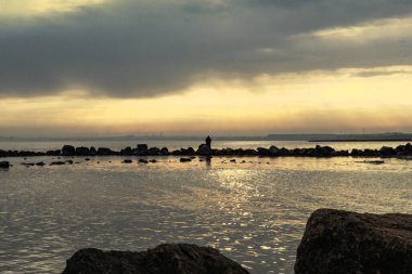 Gün batımı, alçak deniz manzarası, kara bulutlar.
