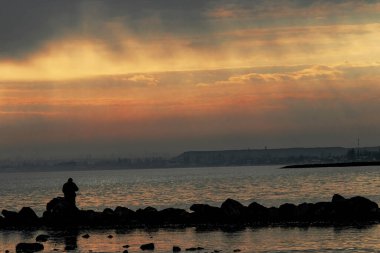 Gün batımı, alçak deniz manzarası, kara bulutlar.