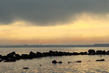 Gün batımı, alçak deniz manzarası, kara bulutlar.