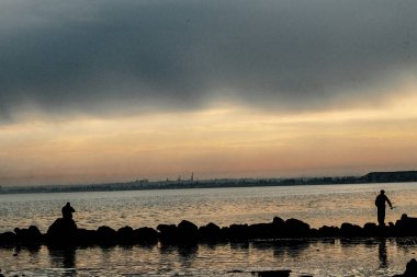 Gün batımı, alçak deniz manzarası, kara bulutlar.