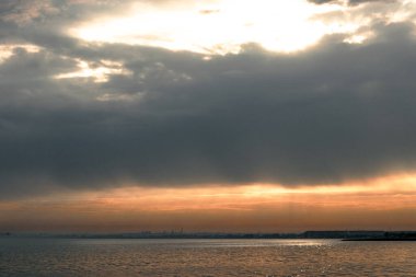 Gün batımı, alçak deniz manzarası, kara bulutlar.