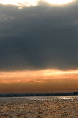 Gün batımı, alçak deniz manzarası, kara bulutlar.
