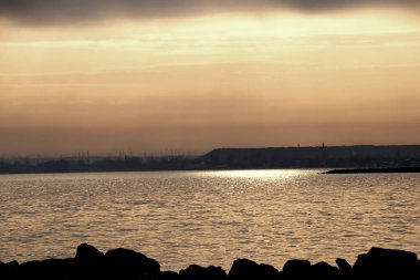 Gün batımı, alçak deniz manzarası, kara bulutlar.