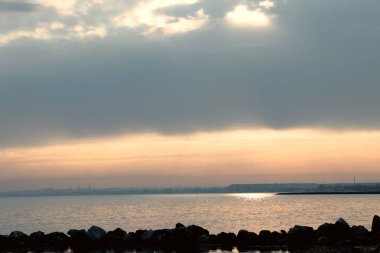 Gün batımı, alçak deniz manzarası, kara bulutlar.