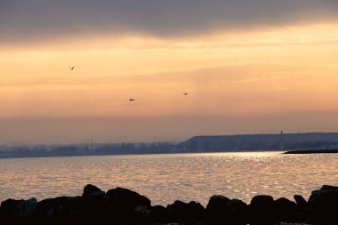 Gün batımı, alçak deniz manzarası, kara bulutlar.