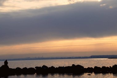Gün batımı, alçak deniz manzarası, kara bulutlar.