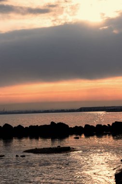 Gün batımı, alçak deniz manzarası, kara bulutlar.