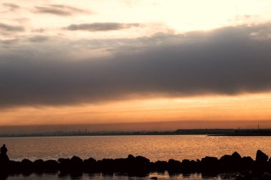 Gün batımı, alçak deniz manzarası, kara bulutlar.