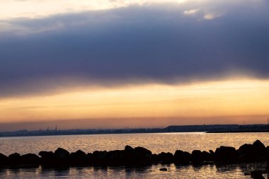 Gün batımı, alçak deniz manzarası, kara bulutlar.