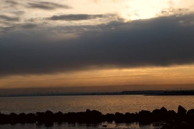 Gün batımı, alçak deniz manzarası, kara bulutlar.