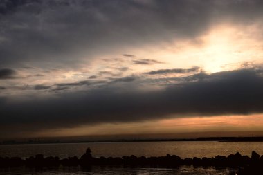 Gün batımı, alçak deniz manzarası, kara bulutlar.
