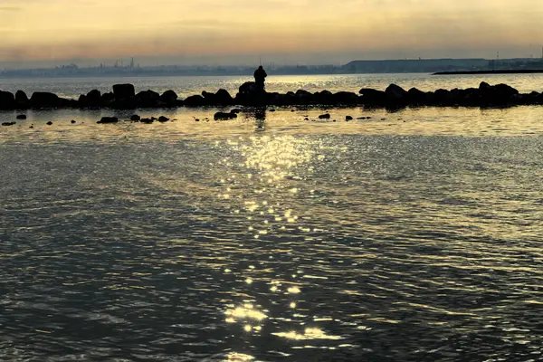 Gün batımı, alçak deniz manzarası, kara bulutlar.