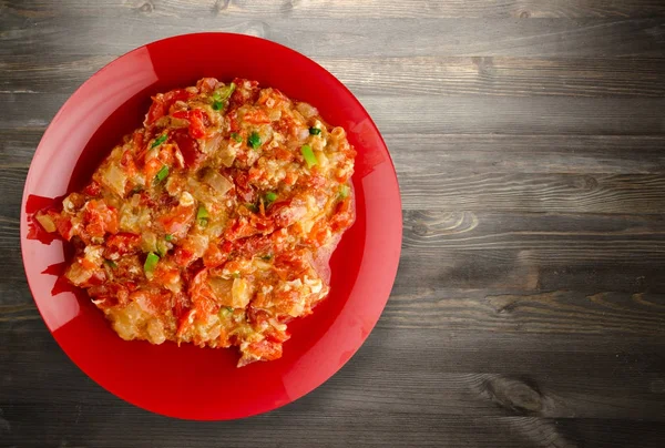 Stewed tomatoes with onions in a plate on a wooden background — Stock Photo, Image