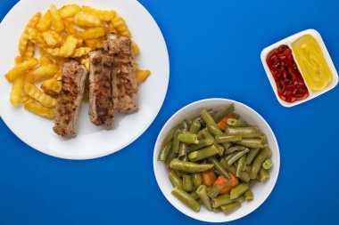 Beyaz tabakta domuz pirzolası ve patates salata ve sosla renklendirilmiş arka planda. Fast food 'un en iyi manzarası. Sağlıksız yiyecekler