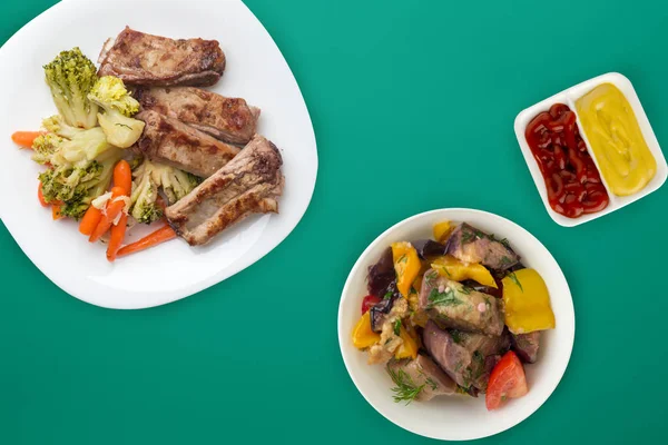 Smažená vepřová žebra s brokolicí, mrkví a česnekem na bílém talíři. smažená vepřová žebírka se zeleninovým salátem na barevném pozadí. vydatné venkovské jídlo horní pohled — Stock fotografie