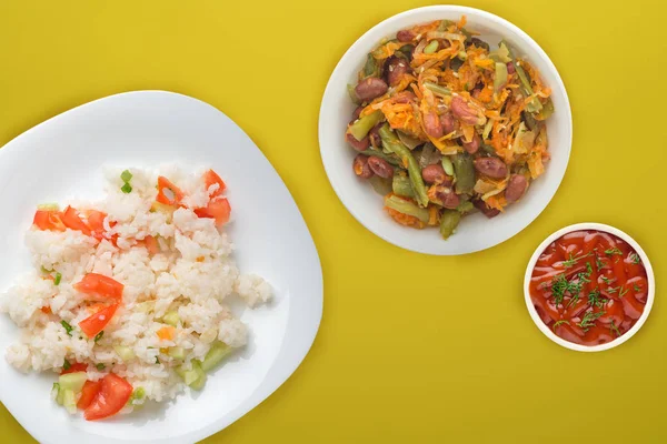 rice with vegetables on a white plate top view, white rice with vegetable salad and sauce on a colored background. rice with tomatoes, cucumbers and onions.