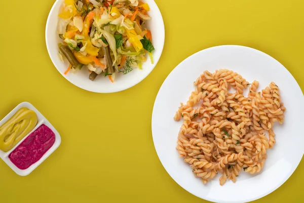 Domates soslu beyaz tabakta makarna ve sebze salatası.