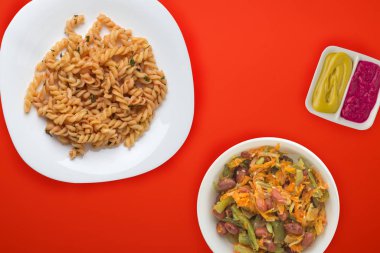 Domates soslu beyaz tabakta makarna ve sebze salatası.