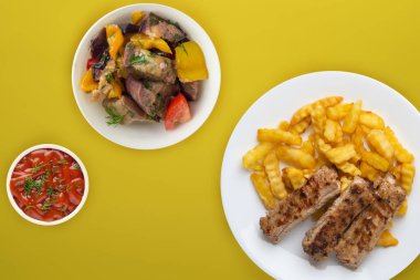 Beyaz bir tabakta salata ve soslu domuz pirzolası ve patates. 