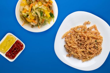 Domates soslu beyaz tabakta makarna ve sebze salatası.