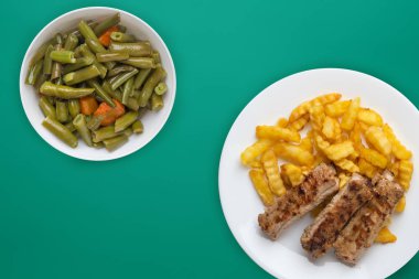 Beyaz bir tabakta salata ve soslu domuz pirzolası ve patates. 