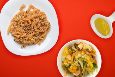 Domates soslu beyaz tabakta makarna ve sebze salatası.