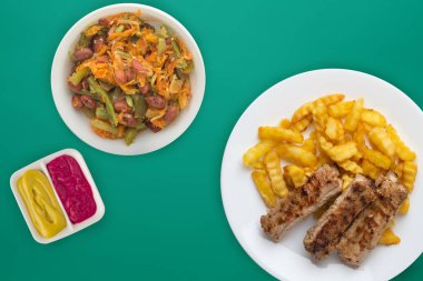 Beyaz bir tabakta salata ve soslu domuz pirzolası ve patates. 