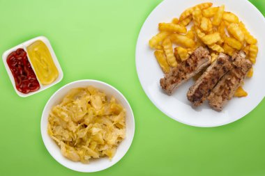 Beyaz bir tabakta salata ve soslu domuz pirzolası ve patates. 