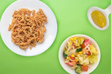 Domates soslu beyaz tabakta makarna ve sebze salatası.