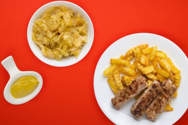 Beyaz bir tabakta salata ve soslu domuz pirzolası ve patates. 