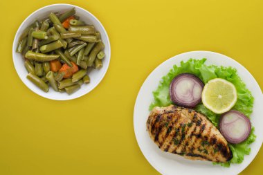 Sebzeli ızgara tavuk, limon, salata, renkli arkaplanda soğan. Tabakta ızgara tavuk filetosu.