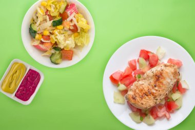 Domates salatası, salatalık ve soğanlı ızgara tavuk göğsü. Koyu kahverengi arka planda beyaz tabakta ızgara tavuk göğsü. Kızarmış tavuk göğsü manzarası