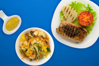 Renkli arka planda patates ve domatesli ızgara domuz eti. Salata ve soslu kızarmış domuz eti.