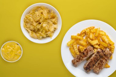 Beyaz bir tabakta salata ve soslu domuz pirzolası ve patates. 