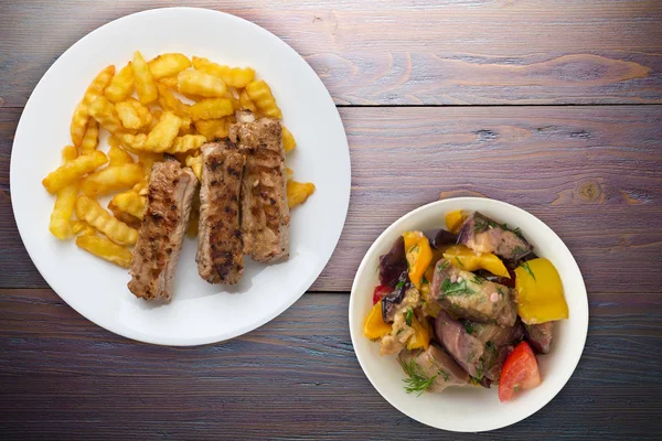 Beyaz bir tabakta salata ve soslu domuz pirzolası ve patates. 