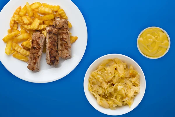 Beyaz bir tabakta salata ve soslu domuz pirzolası ve patates. 