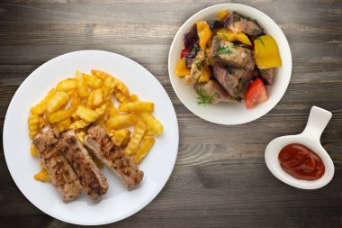 Beyaz tabakta domuz pirzolası ve patates, salata ve ahşap arka planda sos. Fast food 'un en iyi manzarası. Sağlıksız yiyecekler