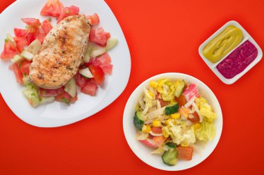 Domates salatası, salatalık ve soğanlı ızgara tavuk göğsü. Koyu kahverengi arka planda beyaz tabakta ızgara tavuk göğsü. Kızarmış tavuk göğsü manzarası