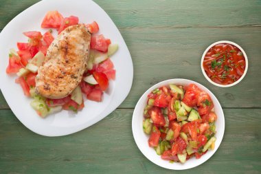 Domates salatası, salatalık ve soğanlı ızgara tavuk göğsü. Koyu kahverengi ahşap arka planda beyaz tabakta ızgara tavuk göğsü. Kızarmış tavuk göğsü manzarası