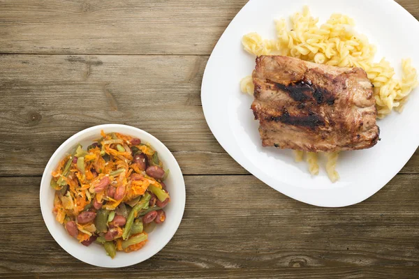 grilled pork ribs with pasta. grilled pork ribs on a white plate on a wooden background.