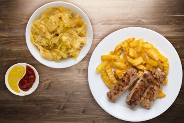 Beyaz tabakta domuz pirzolası ve patates. Kahverengi ahşap arka planda sebze salatası ve sos. Fast food 'un en iyi manzarası. Sağlıksız yiyecekler.