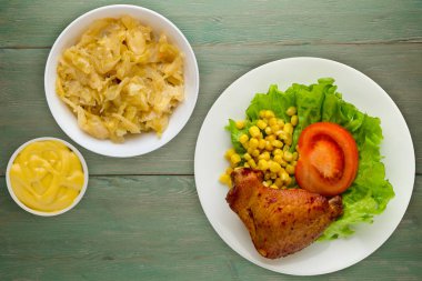 Beyaz tabakta marul, mısır ve domatesli tavuk kanadı. Yeşil ahşap arka plan manzaralı sebze salatası ve soslu tavuk kanadı.