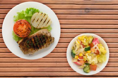  Turuncu ahşap arka planda patates ve domatesle ızgara domuz eti. Salata soslu ızgara domuz eti.