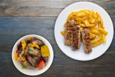 Beyaz bir tabakta domuz pirzolası ve patates ve sebze salatası ve gri mavi ahşap arka planda sos. Fast food 'un en iyi manzarası. Sağlıksız yiyecekler.