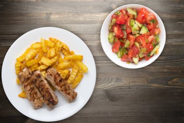 Beyaz tabakta domuz kaburgası ve patates, sebze salatası ve siyah ahşap arka planda sos. Fast food 'un en iyi manzarası. Sağlıksız yiyecekler.