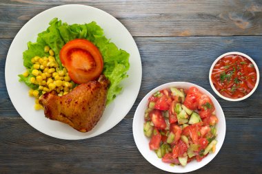 Beyaz tabakta marul, mısır ve domatesli tavuk kanadı. Mavi ahşap arka plan manzaralı sebze salatası ve soslu tavuk kanadı.