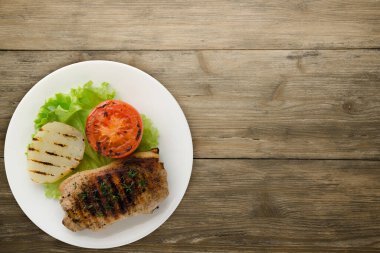  pork grilled with potatoes and tomato on a wooden background. grilled pork on a white plate with salad top view