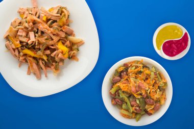 Beyaz tabakta Berlin salatası ve mavi arka planda sebze salatası. Sosis, salatalık, biber soslu salata. .