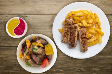 Beyaz tabakta domuz pirzolası ve patates, sebze salatası ve ahşap arka planda sos. Fast food 'un en iyi manzarası. Sağlıksız yiyecekler.